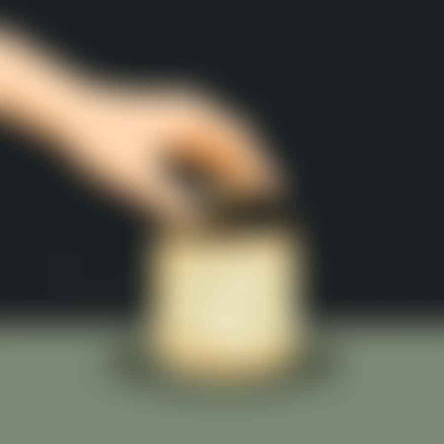 A hand removing leftover wick from an empty candle jar